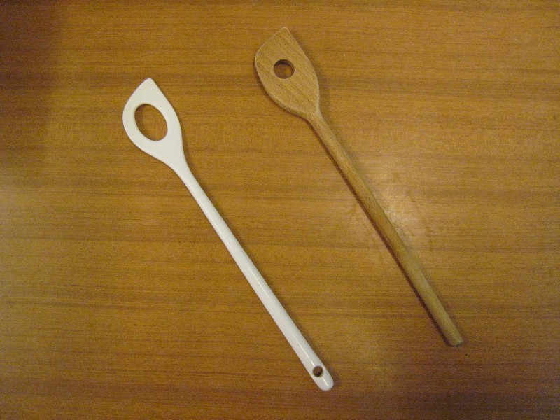 A wooden spoon, a plastic spoon both with a hole